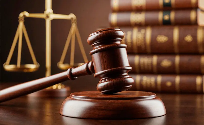 Gavel resting on a wooden block with scales of justice and law books in the background, symbolizing law and justice.