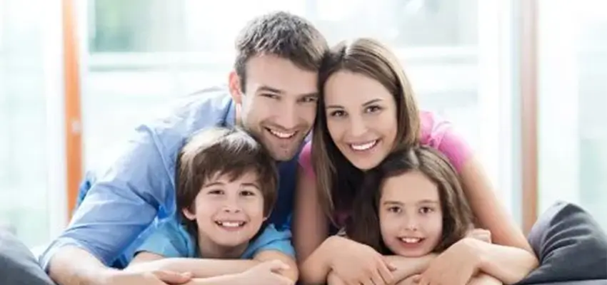 Family of four smiling and hugging on a sofa (parents with two kids).
